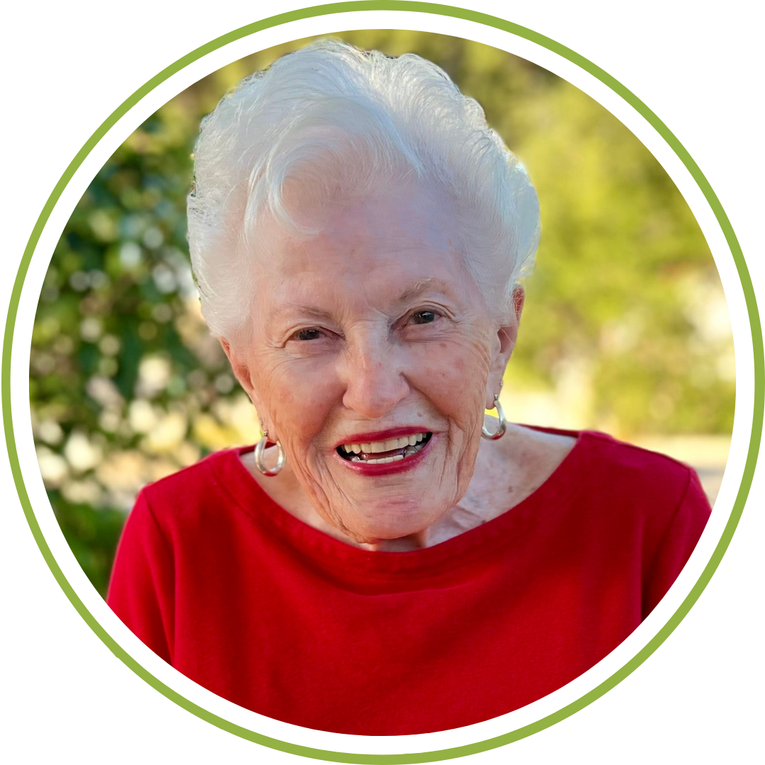 Close-up of longtime Central Coast Zoo supporter Barbie Butz smiling, with vibrant green foliage in the background.